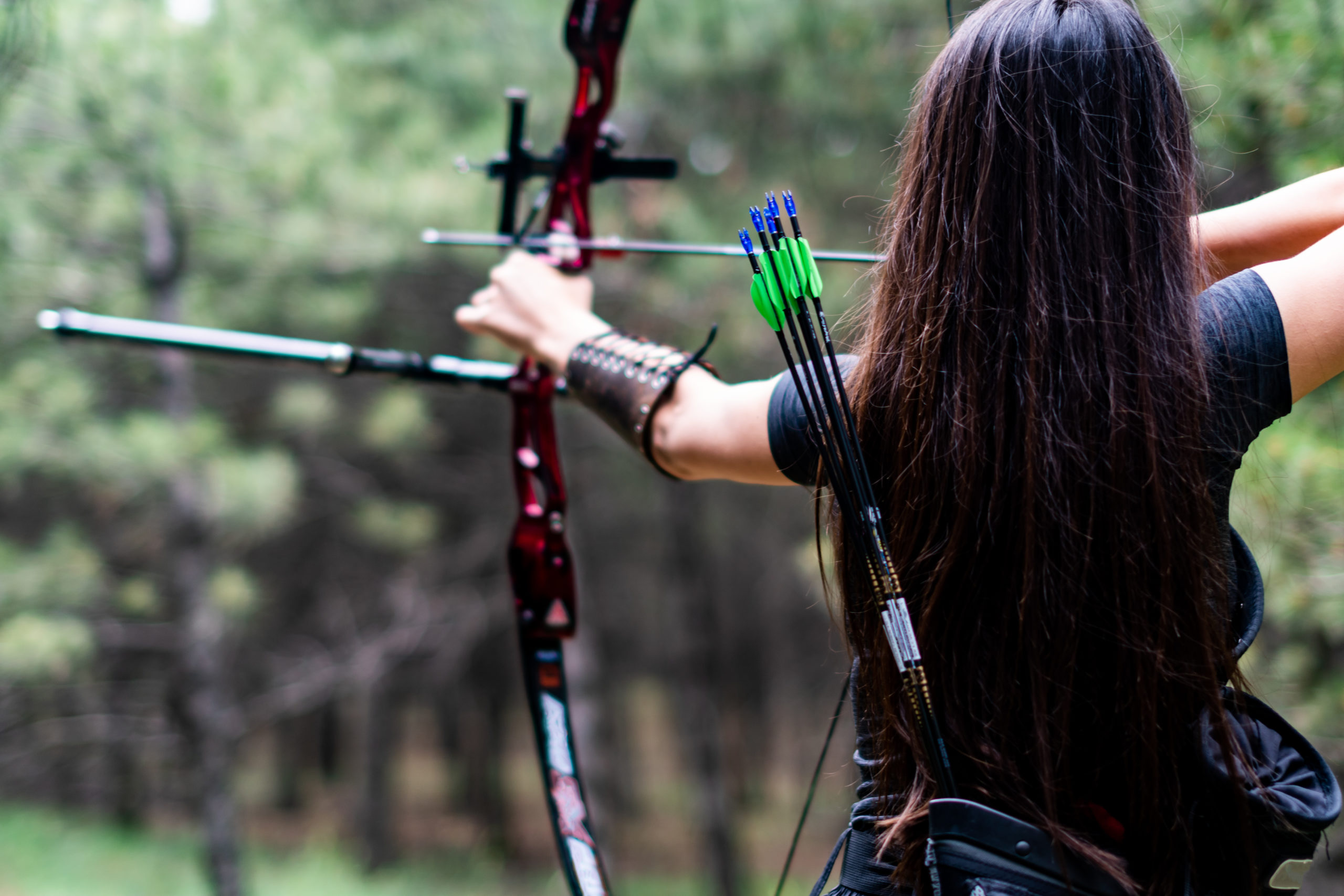 Athletic female aiming with bow and arrow towards the trees